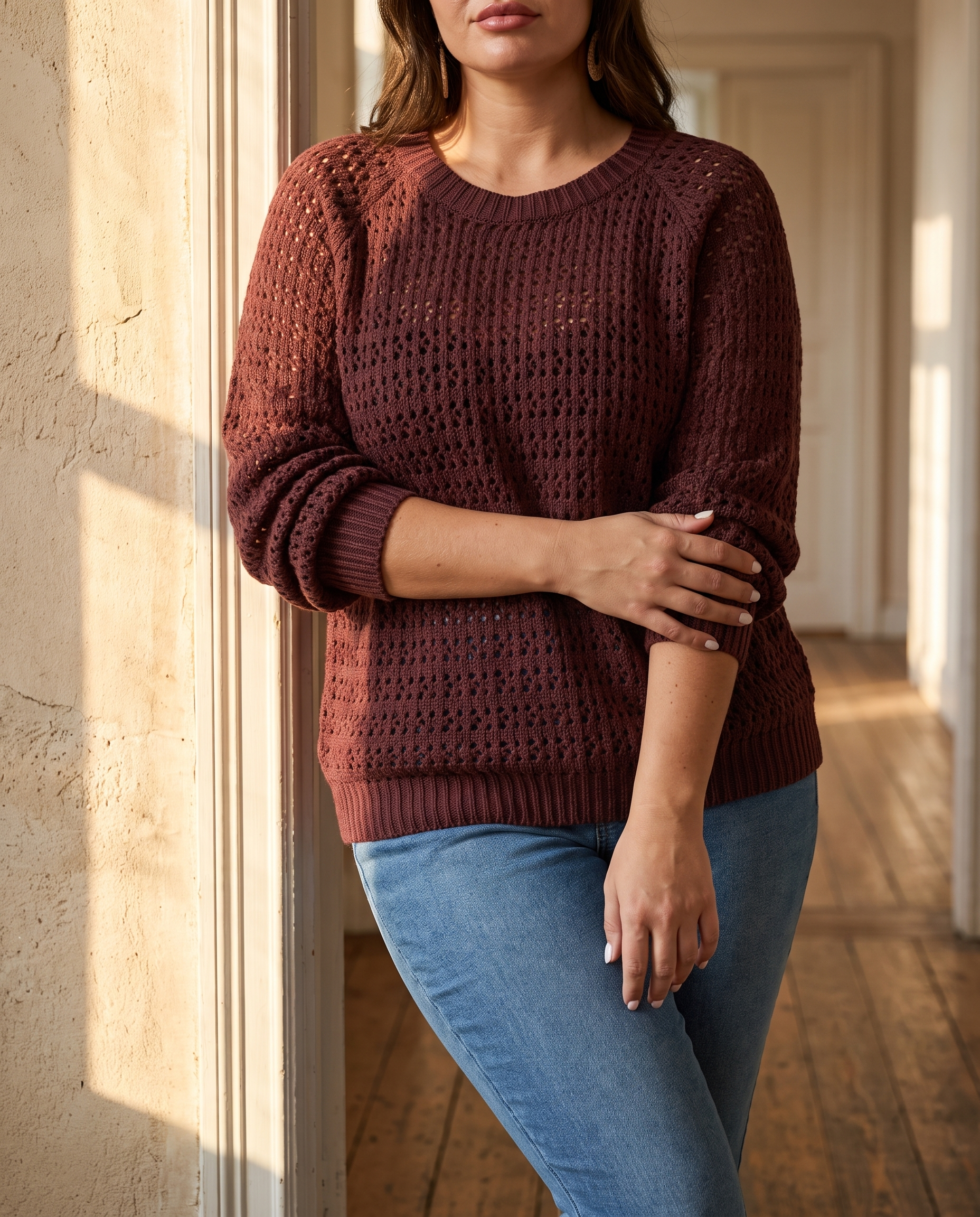 Plus size woman in a plum cable knit cut-out pullover in a sunlit doorway