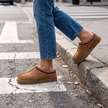 Brown suede slipper clogs worn stepping off a curb into a crosswalk