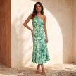 Green floral one shoulder asymmetrical maxi dress worn full length against a sunlit plaster wall