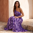 Purple floral one shoulder maxi dress worn seated on a stone step with the skirt pooled