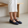 v2 Navy woven Mary Jane flats seated on a light wood bench