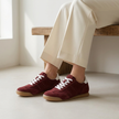 v2 Burgundy Tock suede sneakers seated on a low bench