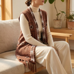 Brown fringe hem sweater vest layered over a cream turtleneck on a sofa