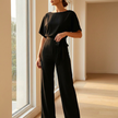Black belted wide leg jumpsuit beside a sunlit window