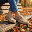 Womens suede clogs seated on a wooden bench with ankles crossed