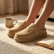 Womens suede slippers resting on a wool rug with coffee and a book