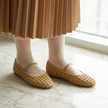 Woven mary jane flats for women worn with a pleated midi skirt on marble