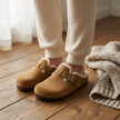 Faux fur lined clogs for women worn on a warm oak floor with a knitted throw