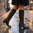 Womens tall block heel boots mid step on a wet city pavement at dusk