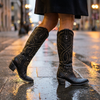 Womens tall block heel boots mid step on a wet city pavement at dusk