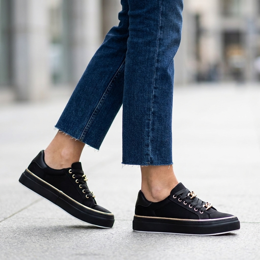 Woman walking in white platform sneakers with gold chain detail