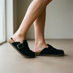 Women's suede slip-on clogs worn on a warm neutral floor in soft daylight
