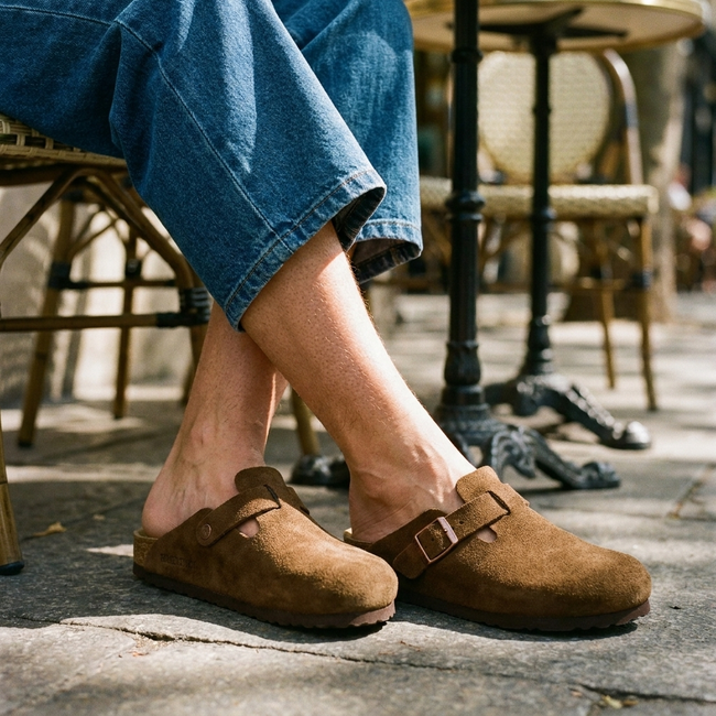 Leather clog mules for women, worn seated at a pavement cafe in dappled light