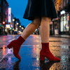 Elegant boots for women mid-stride on a wet city street at dusk with neon reflections