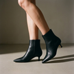 Women's kitten heel ankle booties on a warm grey floor in directional light