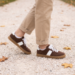 Brown lace up sneakers for women on a gravel park path in fall