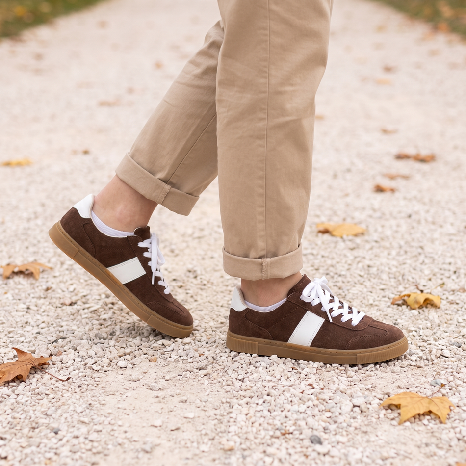 Brown lace up sneakers for women on a gravel park path in fall