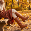 Brown knee high riding boots with buckle detail styled with plaid midi skirt in autumn