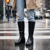 Black knee high riding boots for women with buckle strap and block heel, worn with jeans