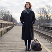 Woman wearing a black long button-front winter coat on a railway platform