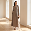 Woman wearing a taupe A-line wrap maxi dress with belt in a sunlit interior