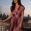 Womens wedding guest dress in rosegold, pleated V neck maxi with cap sleeves, worn at a rooftop reception