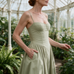 Womens corset midi dress with pockets in sage green, wedding guest A-line dress worn at a botanical glasshouse