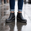 Black waterproof ankle boots worn on a wet city sidewalk